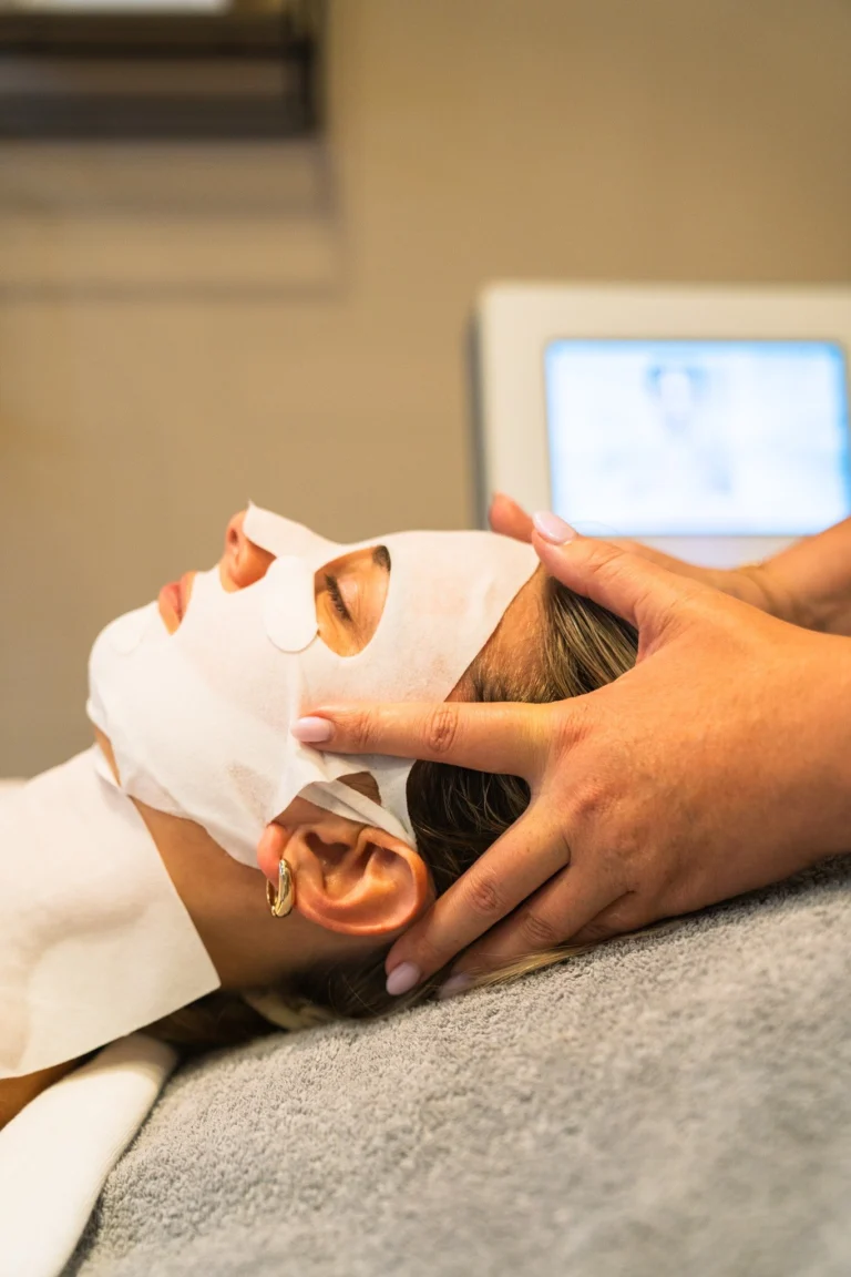 Client wearing a white sheet mask receiving a scalp massage on a treatment bed