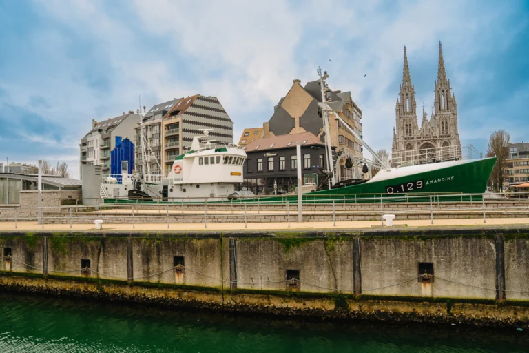 The Amandine seen across the harbour dock, with the spires of St Peter and St Paul's Church behind