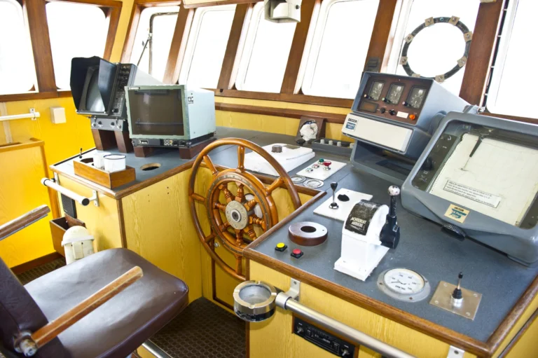Inside the Amandine's yellow wheelhouse with the wooden ship's wheel, radar screens and navigation instruments