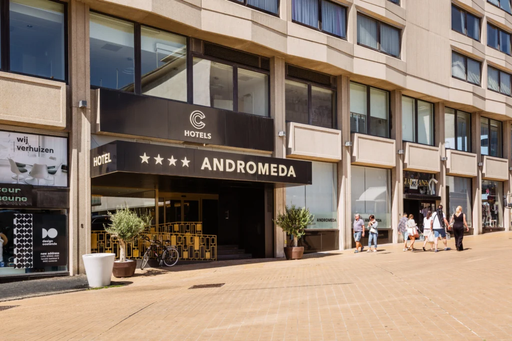 Street-side entrance of the four-star Andromeda hotel, with its dark canopy sign and a terrace on the pavement