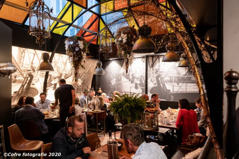 Diners at tables beneath a stained-glass roof, with hanging lanterns and black-and-white harbour murals