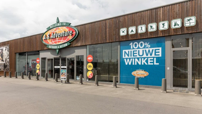 Wood-clad A.S.Adventure store front with the round brand sign, activity pictograms and a large blue '100% nieuwe winkel' banner