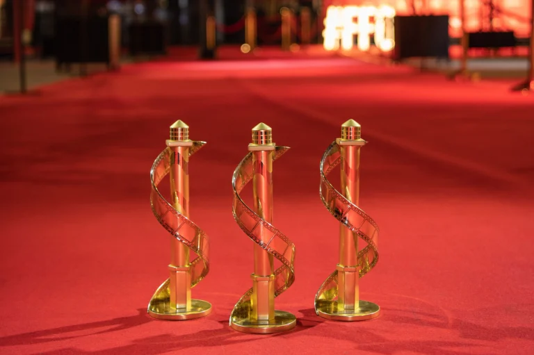Three golden spiral award statuettes standing on a red carpet under warm festival lighting