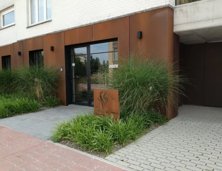 Rust-coloured Corten-steel entrance with glass doors, framed by tall ornamental grasses