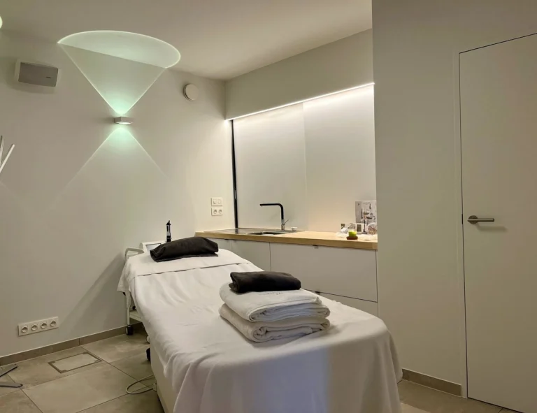 Treatment bed with folded towels in a white room with built-in cupboards and wall lights