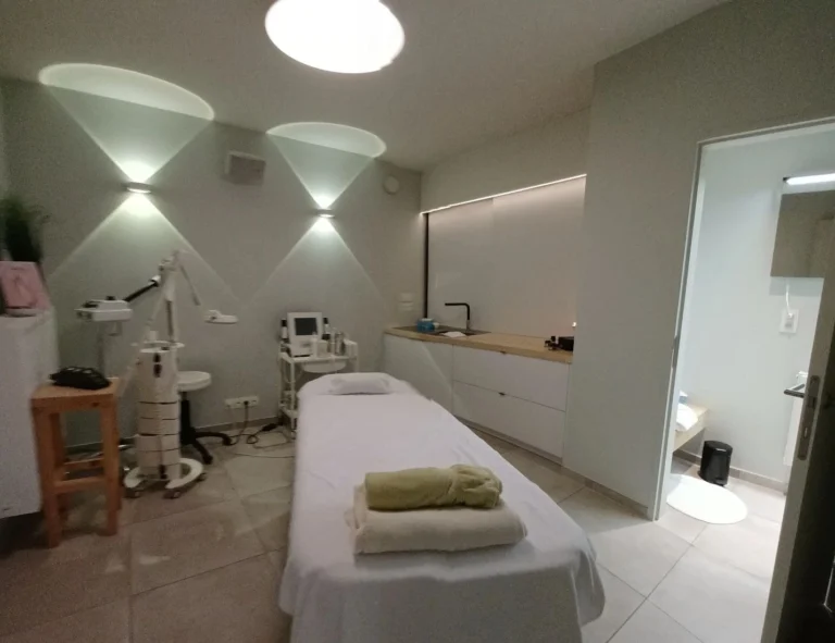Minimalist treatment room with a towel-covered treatment bed, a facial steamer and soft cone-shaped wall lights