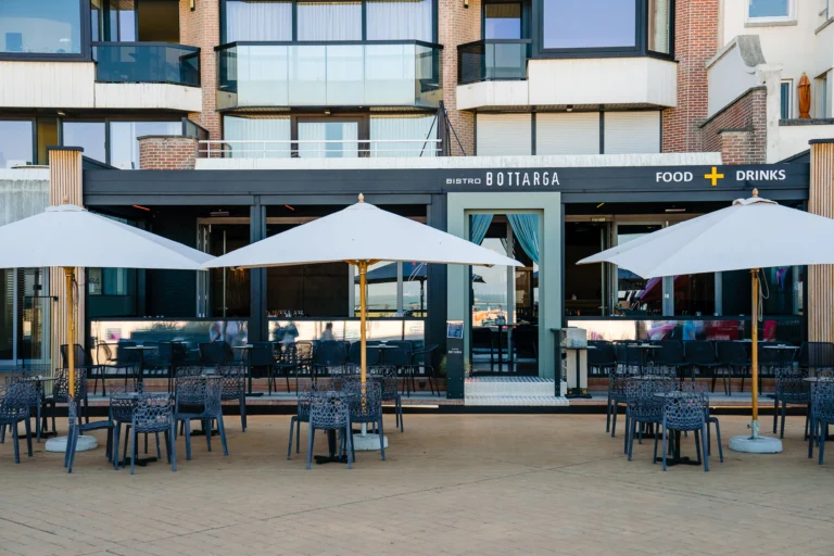 Frontage of Bistro Bottarga on the Albert I-promenade, with tables and parasols on the terrace in front of the glass-fronted restaurant