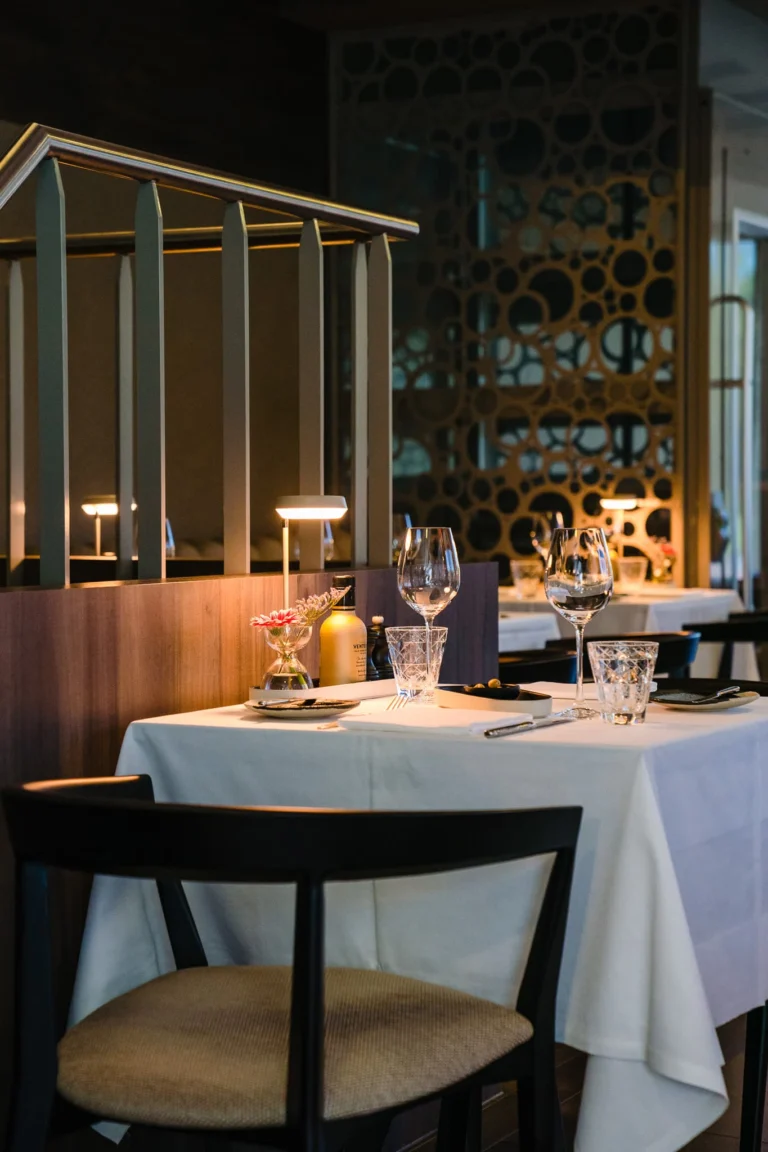 Table laid with white linen, glasses and small lamps in front of a brass screen with circular cut-outs