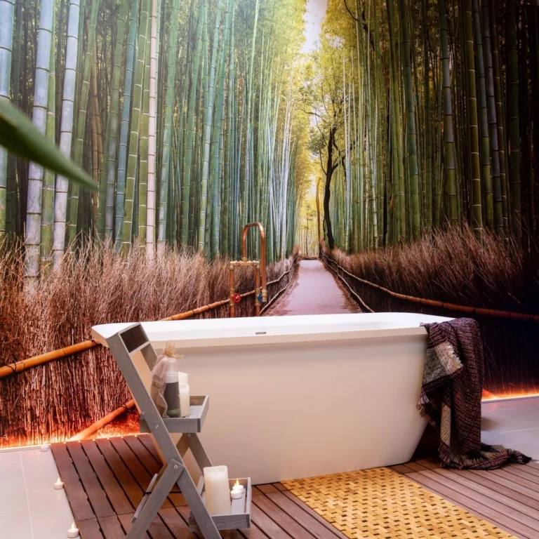 Freestanding white bath on a wooden deck in front of a bamboo-forest wall mural, with candles beside it