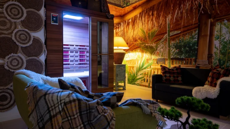 Relaxation lounge with rattan decor, plaid-covered sofas and a lit infrared sauna cabin