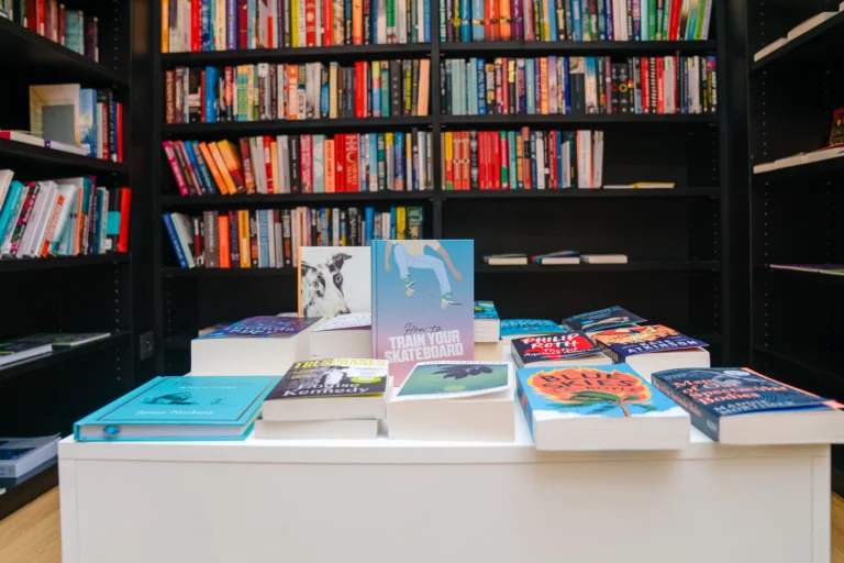 White display table stacked with new books in front of black shelves full of colourful spines