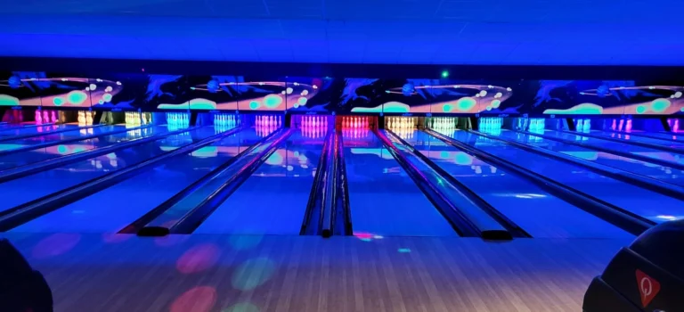 Row of bowling lanes lit in blue and neon light, with glowing pins at the far end