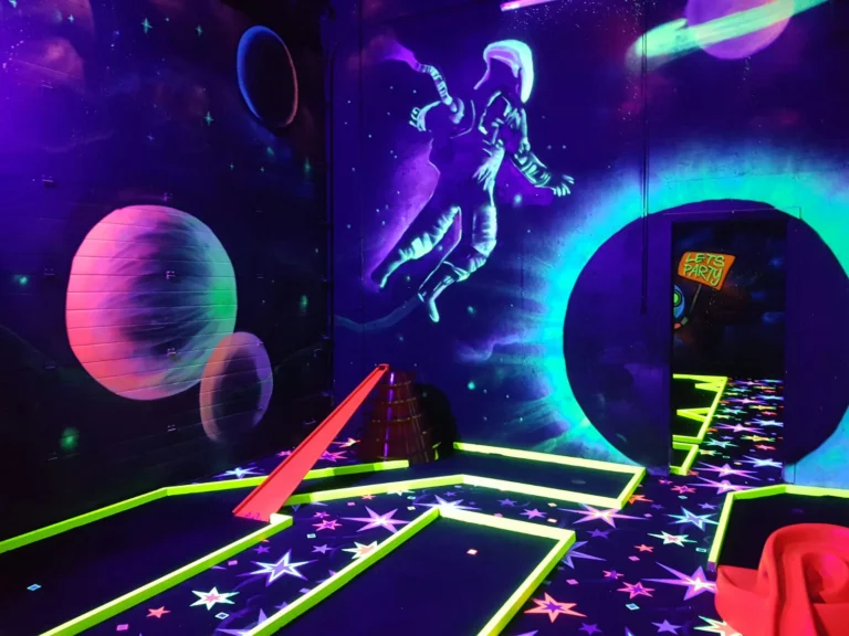 Glow-in-the-dark minigolf course with space-themed murals of planets and an astronaut