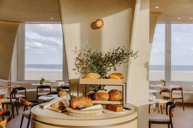 Light breakfast room with a round bread table and large windows looking out over the beach and sea