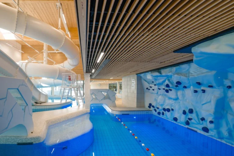 Shallow pool lane beside an ice-themed climbing wall, with water slides winding above