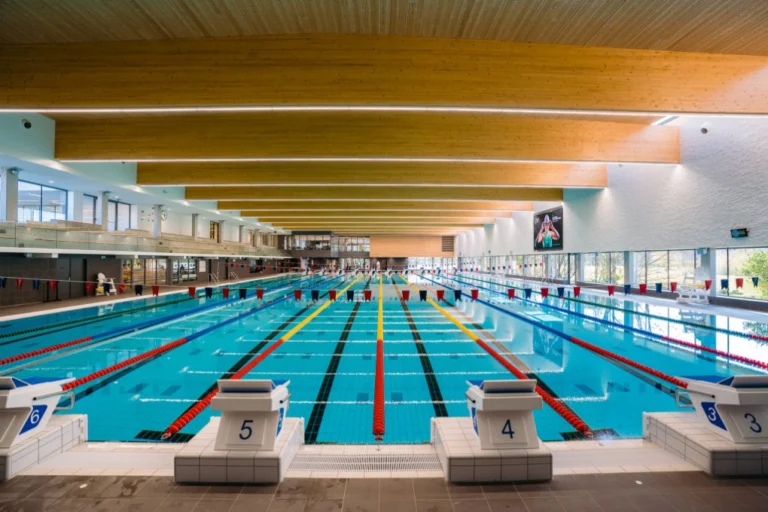 Indoor competition pool with lane ropes, numbered starting blocks and a timber-beamed ceiling