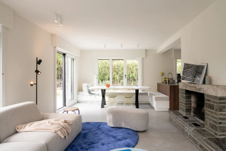 Open living area with a stone fireplace, sofa, blue rug and dining table by the garden doors