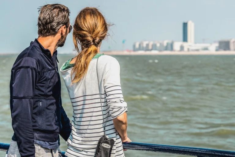 Couple seen from behind at the railing, watching the seafront apartment blocks from the water