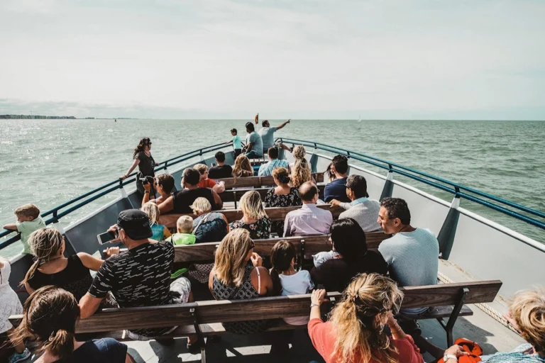 Passengers seated on wooden benches on the open foredeck as the boat heads out to sea