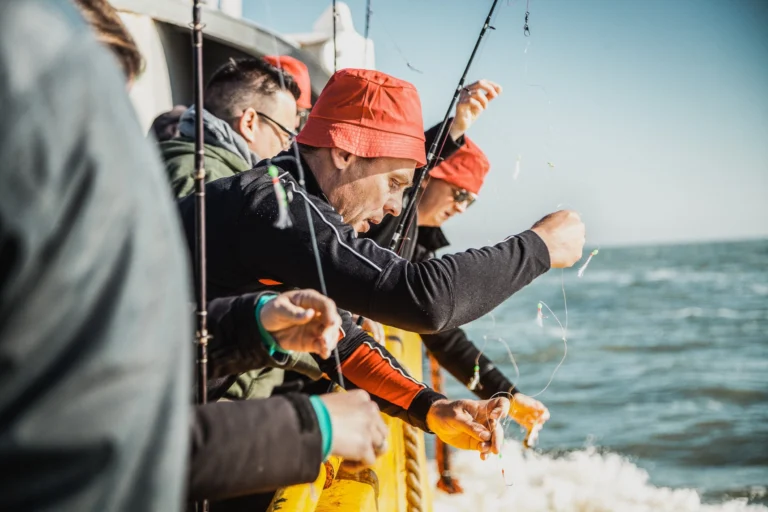 Anglers in red hats preparing baited lines over the side of the fishing boat at sea