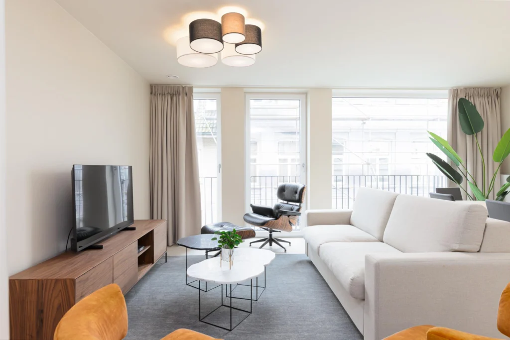 Bright apartment living room with a cream sofa, leather lounge chair, marble coffee tables and tall windows