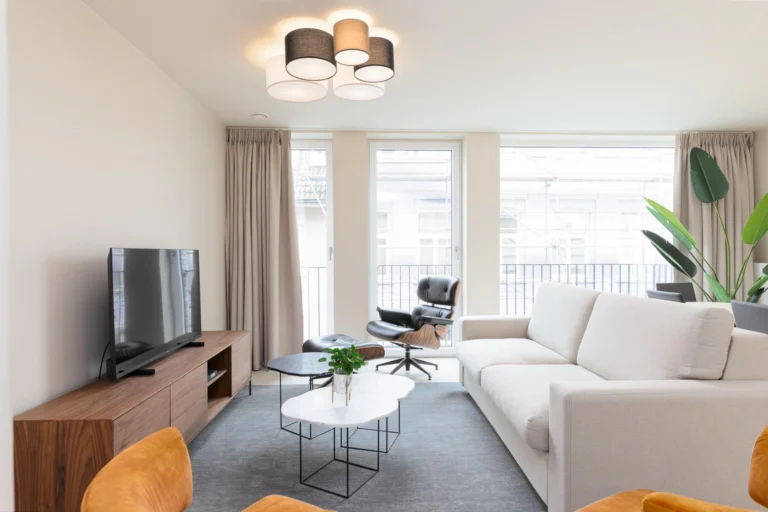 Bright apartment living room with a cream sofa, leather lounge chair, marble coffee tables and tall windows