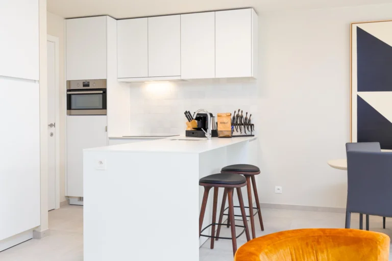 White open-plan kitchen with a breakfast bar, two wooden stools and a built-in oven