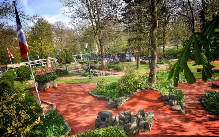 Minigolf holes with rock edging and a little cottage obstacle, flags flying among spring trees