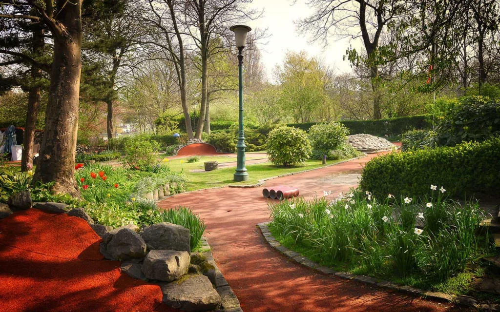 Red minigolf lanes winding between rocks, tulips and shrubs under the trees of Leopold Park