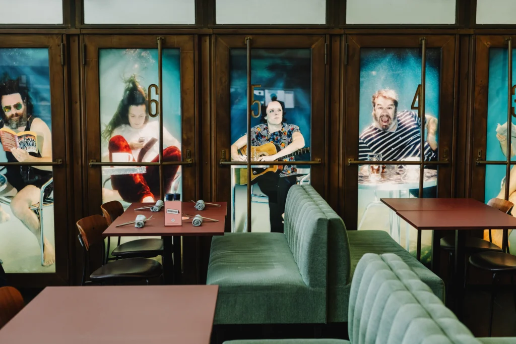 The dining room with green banquette seating and red-brown tables in front of tall glazed doors dressed with large portrait panels