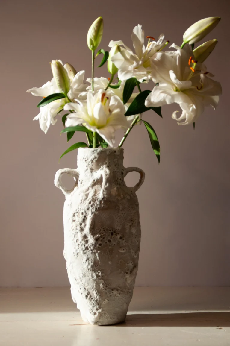 Rough-textured white ceramic vase with two handles holding a bunch of white lilies