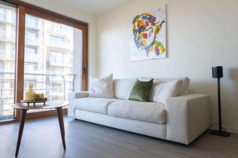 Living room with a white sofa, a colourful portrait painting and full-height balcony windows