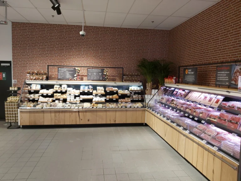 Refrigerated cheese and meat counters with wooden fronts against a red-brick wall