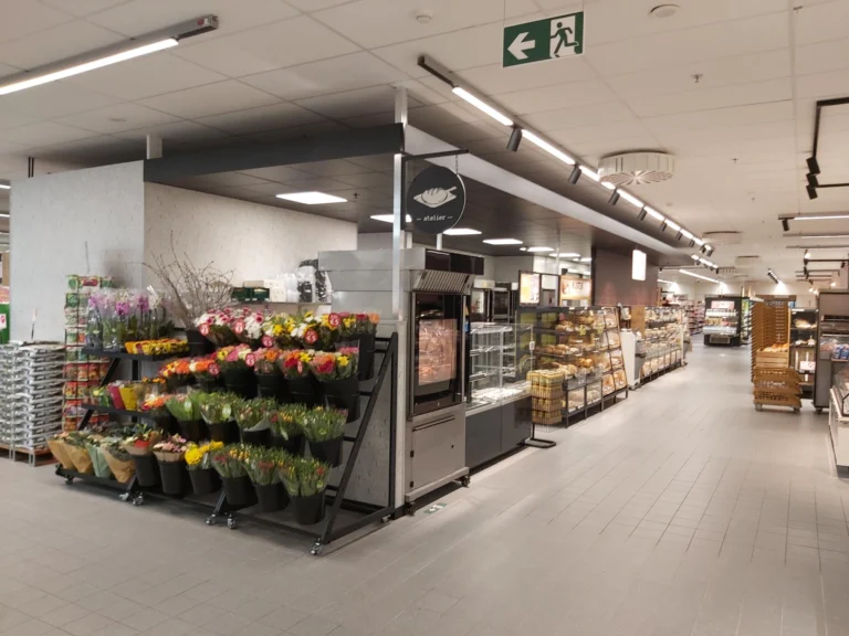 Supermarket interior with a stand of cut flowers and potted plants beside a long, bright aisle
