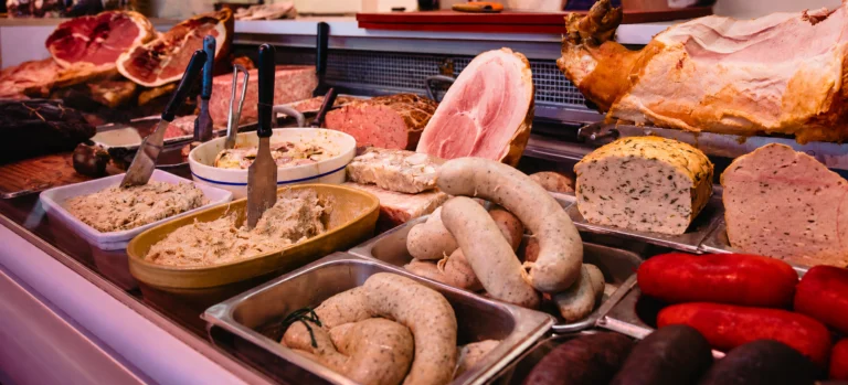 Charcuterie counter with hams, pâtés, white sausages, red sausages and bowls of spread with knives