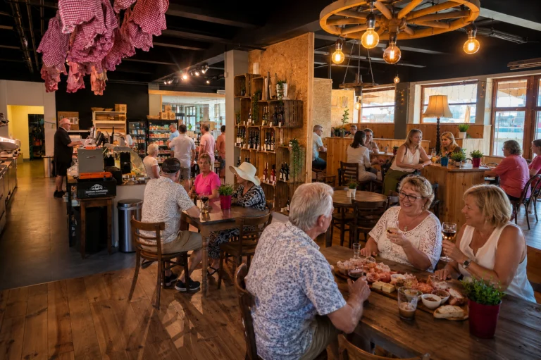 Wood-panelled shop and tasting room with shelves of bottles, a cart-wheel chandelier and visitors eating at tables