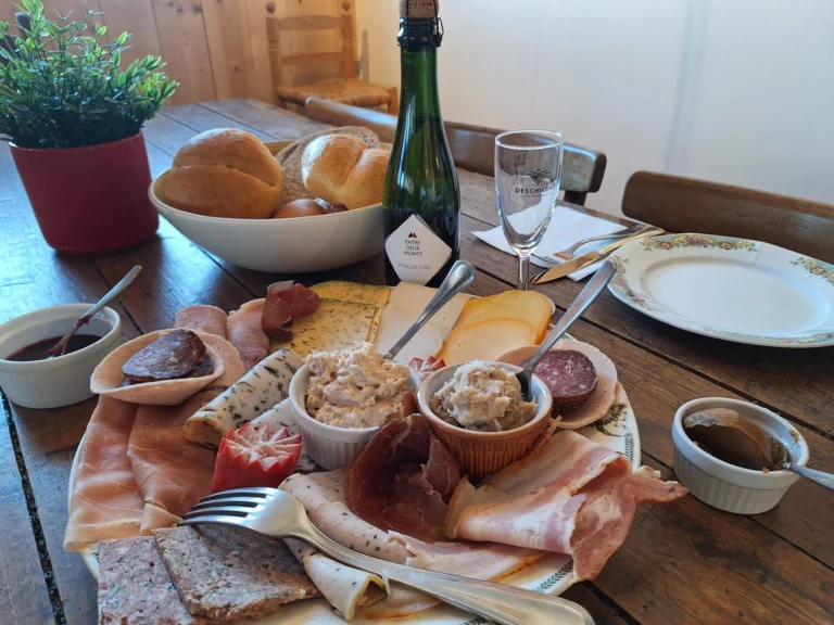 Tasting plate of sliced ham, sausage, pâté and cheese with spreads and mustard, bread rolls and a bottle on a wooden table
