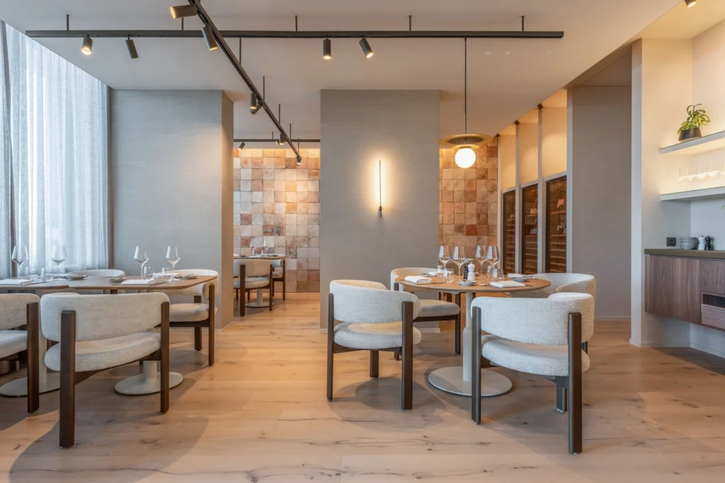 Light dining room with cream bouclé chairs, an oak floor, a terracotta tile wall and wine cabinets