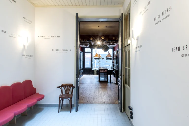 Entrance hall with a red bench and painters' names on the walls, opening onto the old shell shop