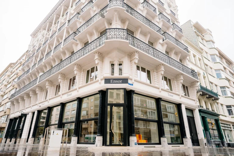 White corner building of the James Ensor House with wrought-iron balconies and tall black shopfront windows