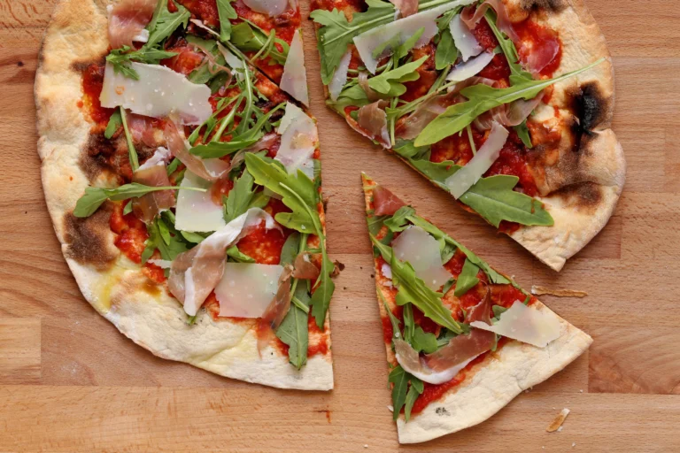 A thin-crust pizza topped with rocket and shaved parmesan on a wooden board