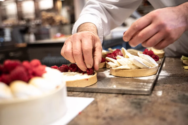A pastry chef placing raspberries on small tarts on a work surface