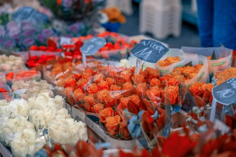 Rows of orange roses, white chrysanthemums and red bouquets with price tags at a flower market stall