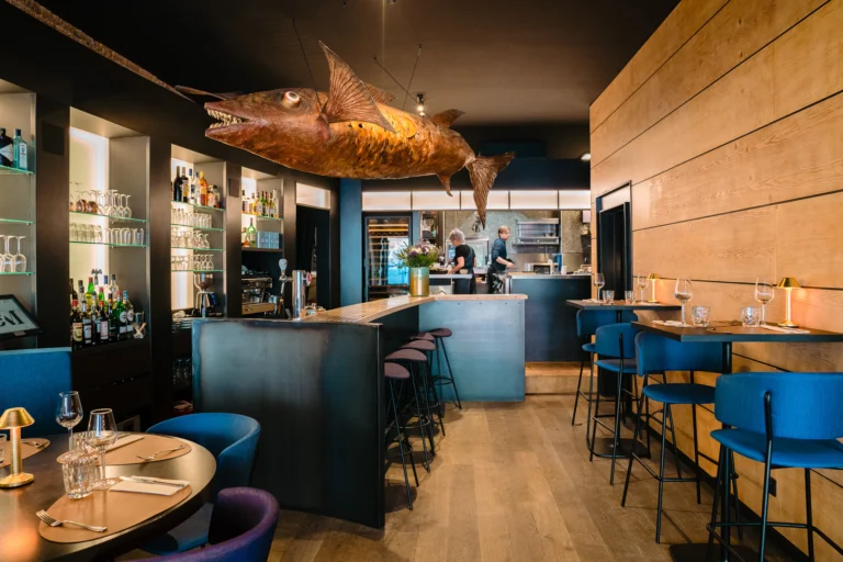 Bar and dining room with a wood-panelled wall, high stools at the bar and a large fish sculpture hanging from the ceiling