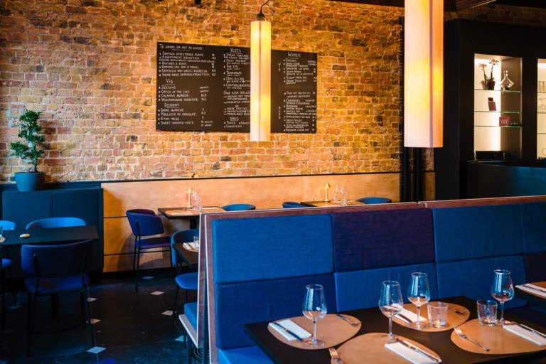 Exposed brick wall with a blackboard menu above blue banquettes and laid tables