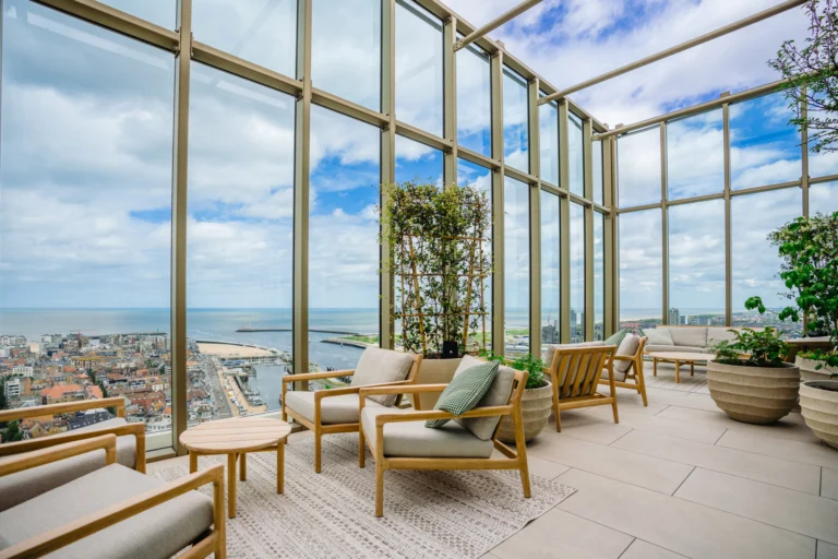 A glass-walled lounge high in the tower with wicker armchairs and a view over Ostend's rooftops and the sea