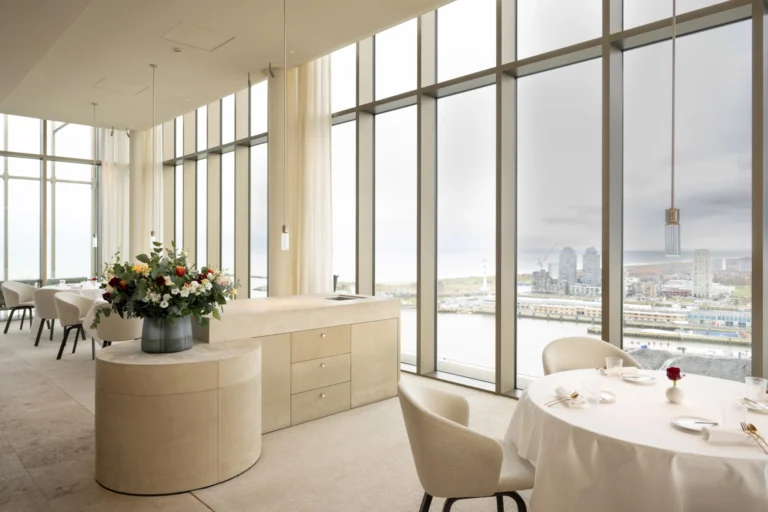 The pale dining room of Haut with floor-to-ceiling windows, tables laid with white cloths and a view over the harbour and town