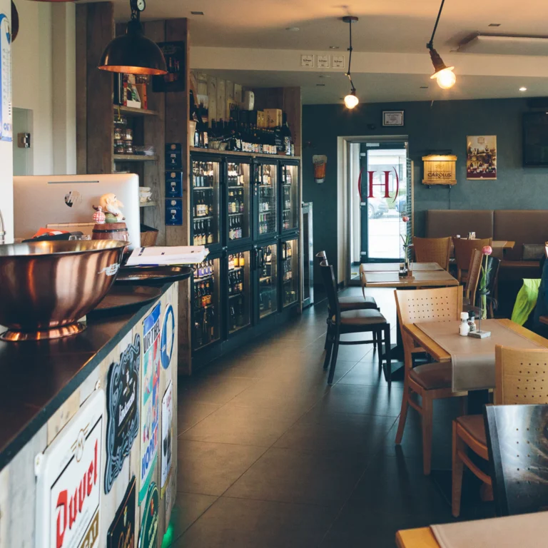 The dining room at Heerlijk, with a bar and fridges of bottled beer on one side and wooden tables and chairs along a banquette