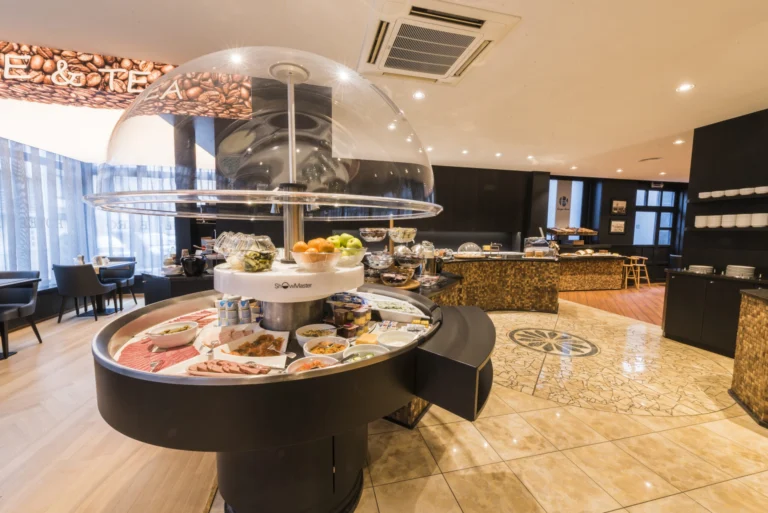 Round breakfast buffet island under a glass dome with breads, cheeses and fruit in the breakfast room