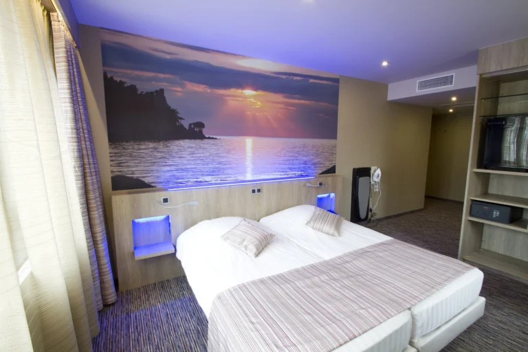 Hotel room with twin beds pushed together beneath a large photo mural of a sunset over the sea